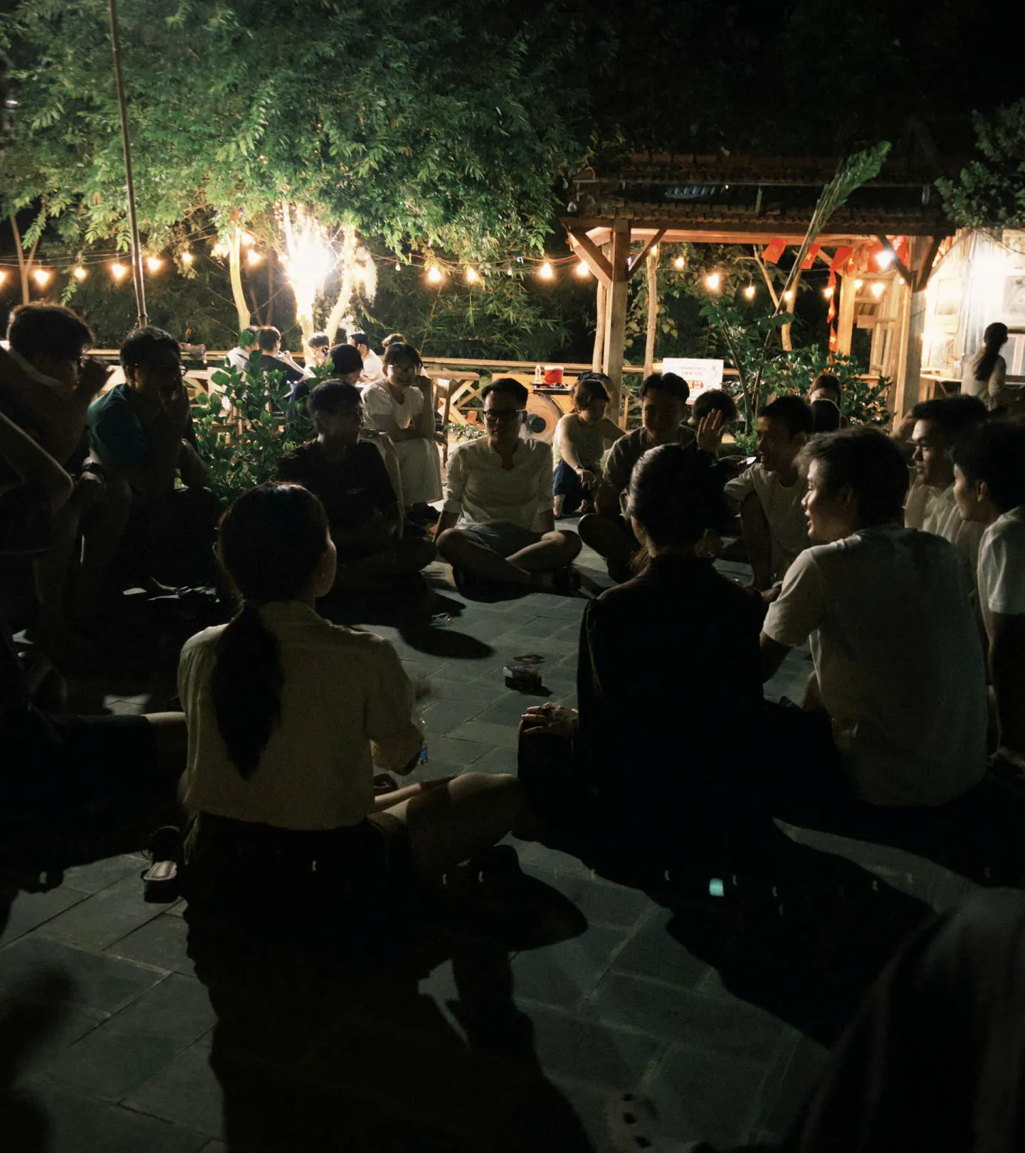 Buổi tối ngoài trời, mọi người quây quần dưới dây đèn